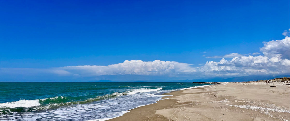 Spiaggia del Gombo nel Parco di San Rossore Zona Rossa deserta e selvaggia con cielo azzurro e nuvole bianche.